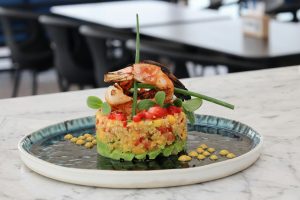Vibrant shrimp dish with quinoa, avocado, and microgreens elegantly presented on a ceramic plate.