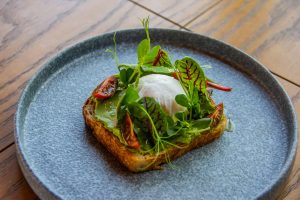 Delicious avocado toast topped with fresh greens and a poached egg, served on a rustic ceramic plate.