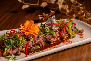Deliciously plated beef tataki garnished with fresh herbs and vibrant edible flowers.