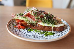 A gourmet open-faced sandwich topped with fresh greens and cured meat on a patterned plate.