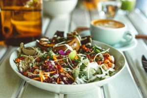 Colorful vegetarian salad with a latte on a white table, captured in a cozy indoor setting.