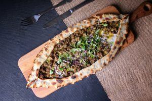 Delicious Turkish pide topped with vegetables and fresh herbs on a wooden board.