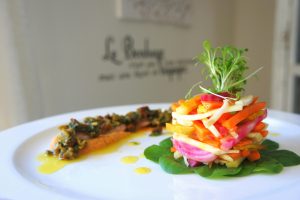 A vibrant stack of fresh vegetables artfully plated, served with a gourmet dressing.