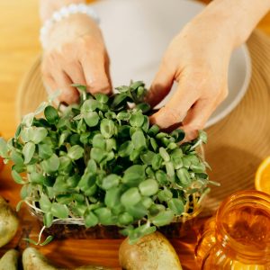 Close up of hands arranging fresh greens with pears on a wooden kitchen table.