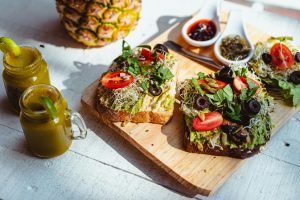 Close-up of fresh avocado toast with toppings, served with juices on a wooden board.