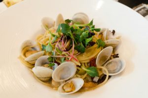Close-up of a plate of spaghetti with clams and microgreens, highlighting gourmet presentation.